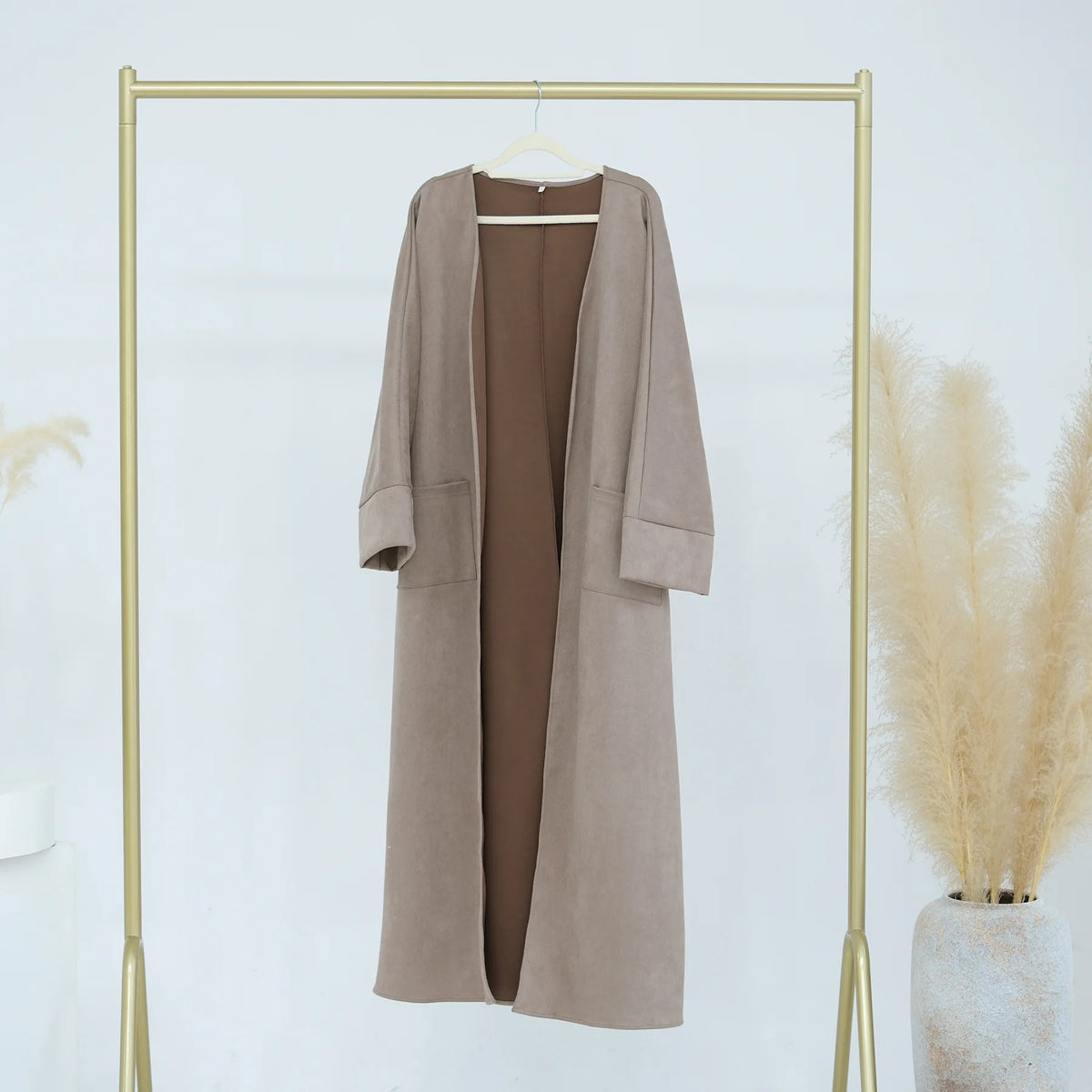 A beige women's abaya trench coat displayed on a gold hanger against a white background.