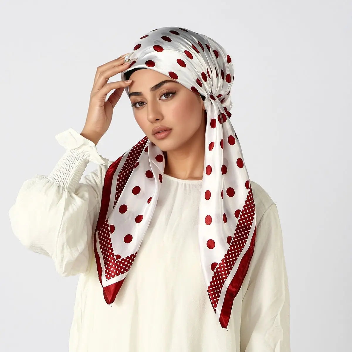 Eine Frau trägt einen weißen Seiden-Turban-Hijab mit roten Polka Dots um ihren Kopf.