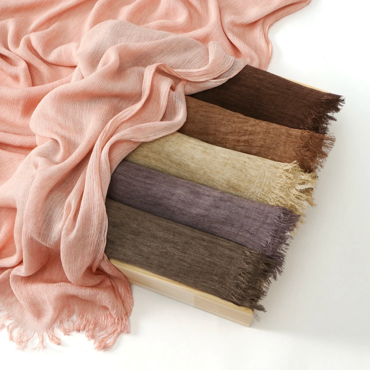 Une pile de foulards ou hijabs en rayon et marron à crinkle en rayonne, exposés sur une surface blanche.