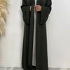 Eine Frau trägt ein fließendes, dunkel olivgrünes Abaya-Kaftan mit offenem Vorderteil und weißer Unterkleidung.
