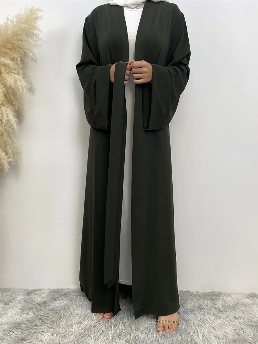 Eine Frau trägt ein fließendes, dunkel olivgrünes Abaya-Kaftan mit offenem Vorderteil und weißer Unterkleidung.