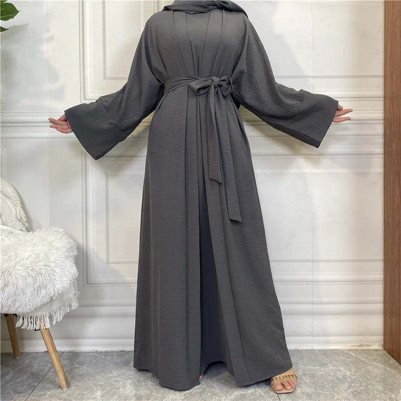 A full-length, charcoal gray elegant women's abaya and kaftan set displayed against a white paneled wall.