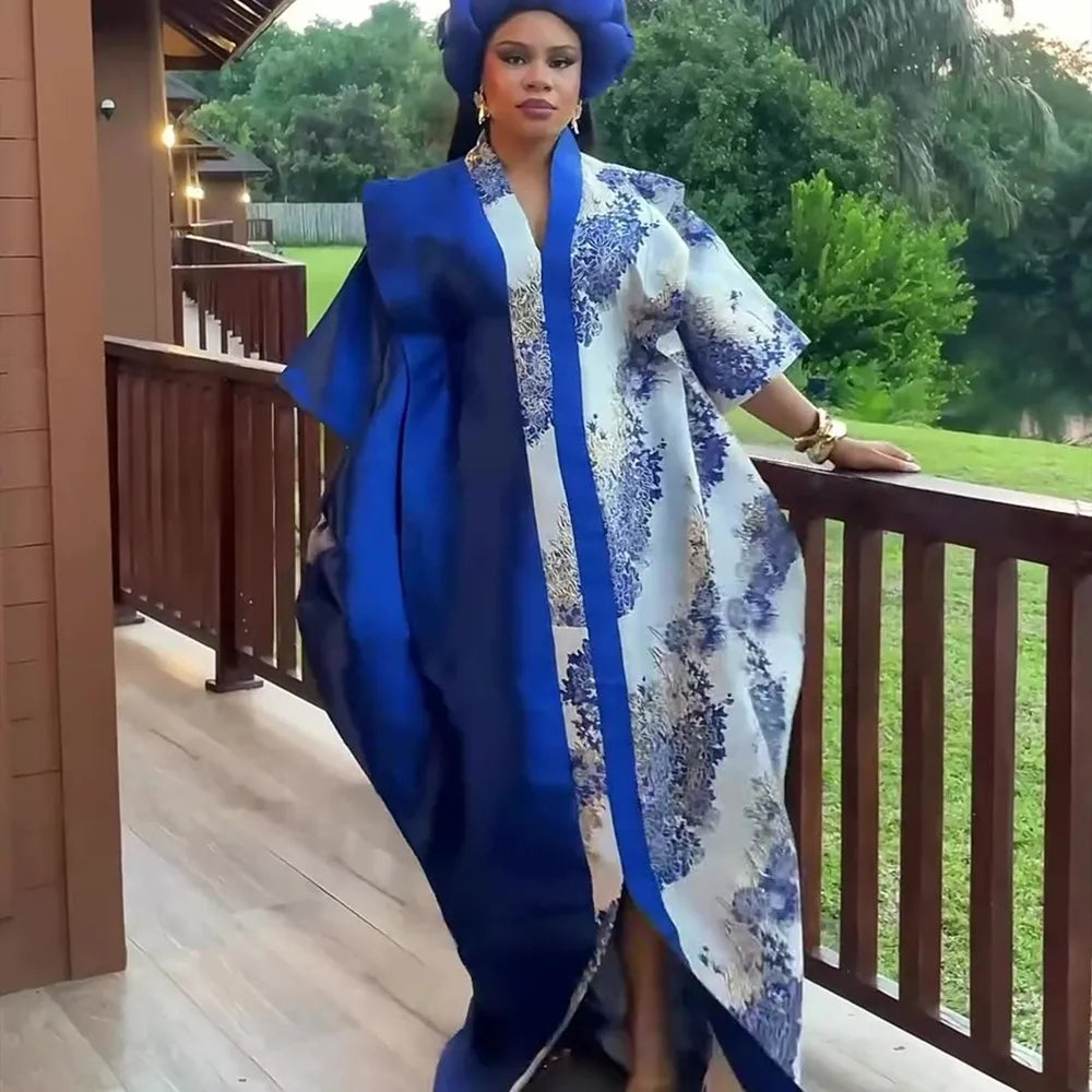 A woman wearing an elegant blue and white patterned kaftan with a matching blue head wrap standing on a wooden porch.