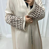Une femme portant une élégante abaya beige à manches brodées et un haut noir, tenant un téléphone.