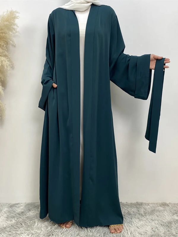 A dark teal flowy open-front abaya kaftan worn by a woman, featuring long sleeves and a white inner garment.