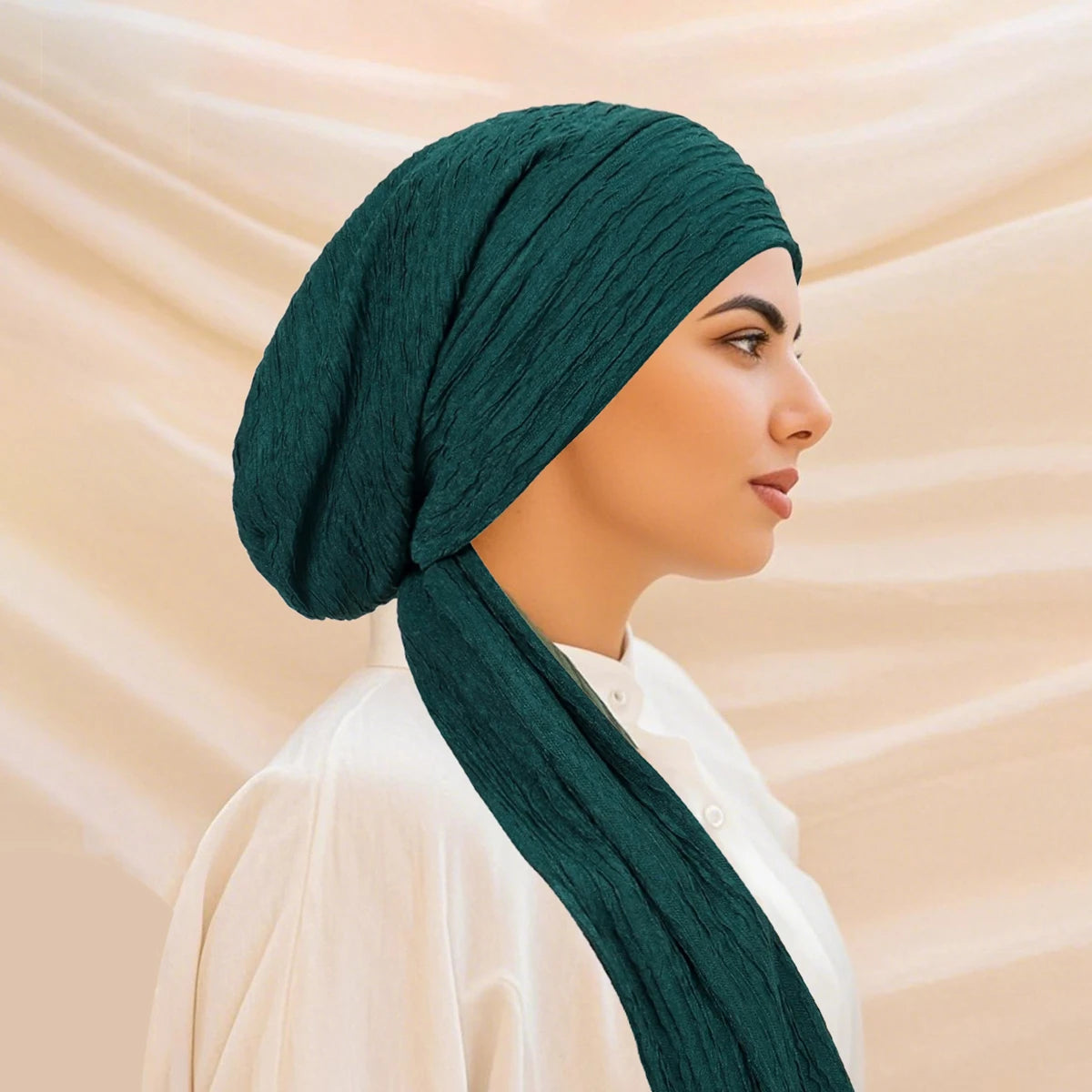 A woman wearing a dark emerald green solid color turban hijab cap and white clothing.