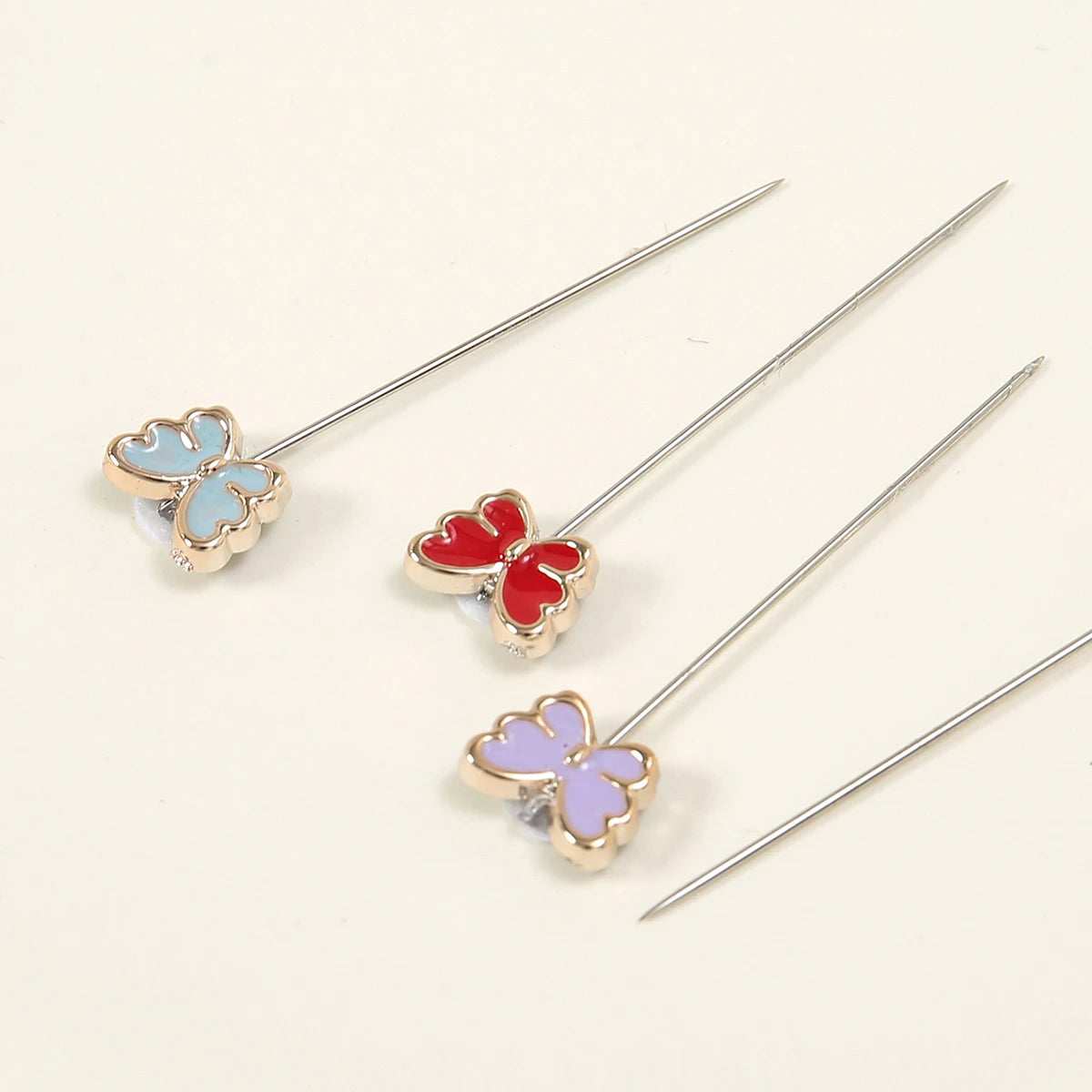 Un juego de tres devanadores para hijab de seda con estampado de mariposa plateada y detalles florales.