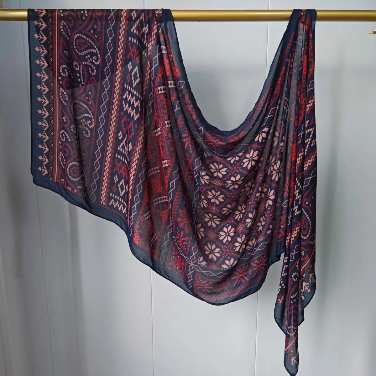 Dunkelrot-blau gemusterter Hijab-Schal hängt an einem Holzstab.