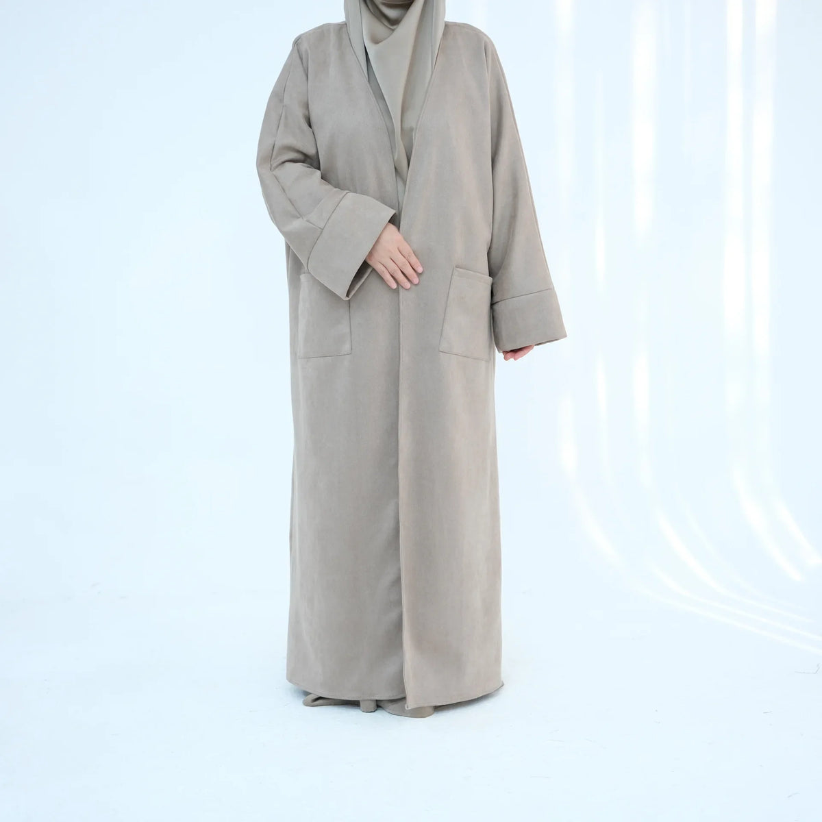 A full-length shot of an elegant women's beige abaya trench coat worn by a model against a white background.