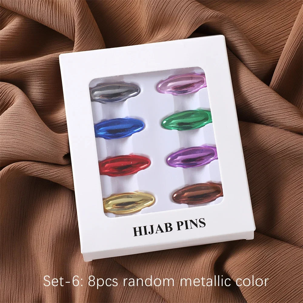 Set von sechs zufälligen metallfarbigen Hijab-Pins in einer weißen Box auf braunem Stoff