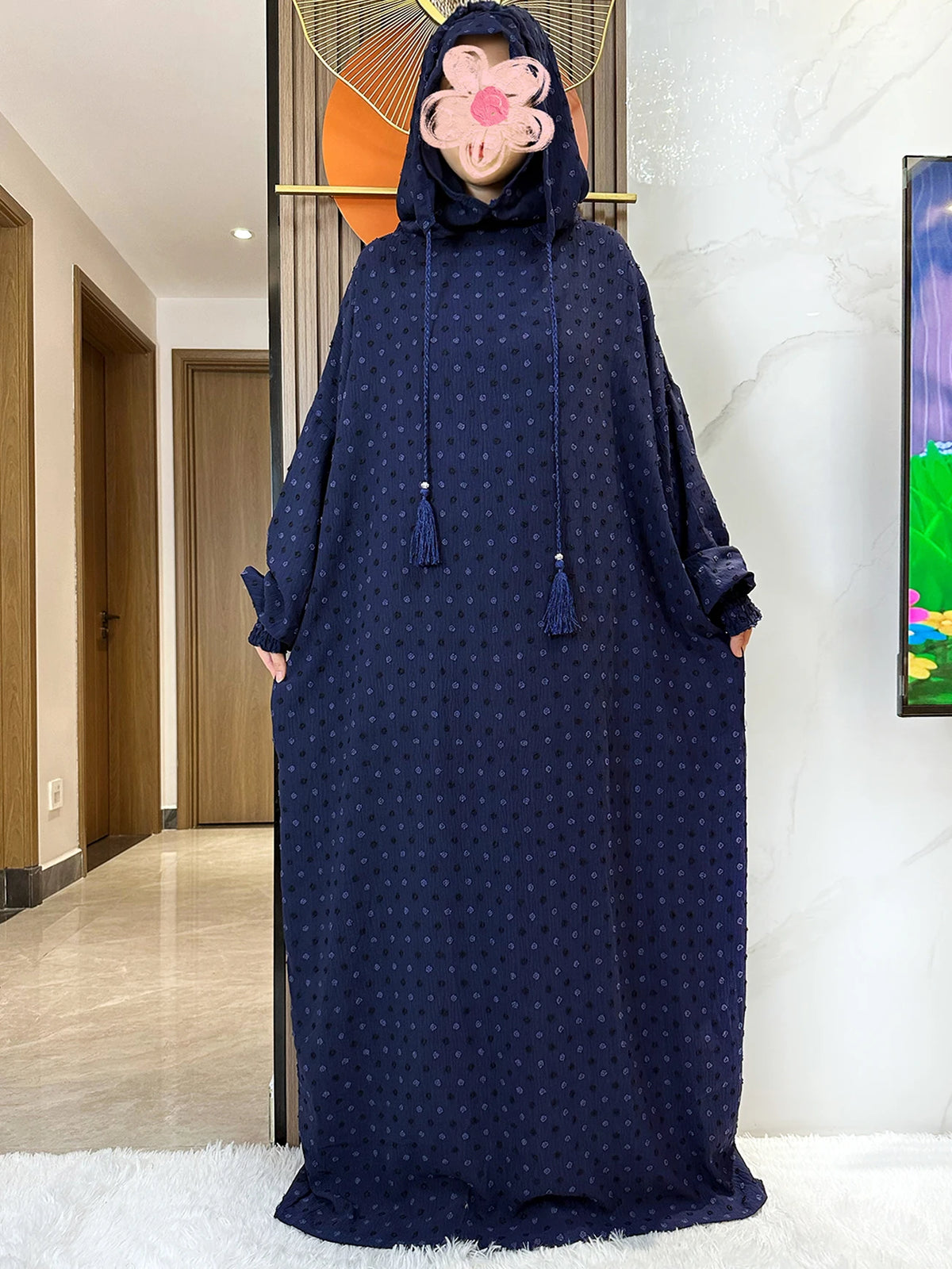 Una abaya de algodón azul oscuro con capucha y flecos decorativos exhibida en interiores.