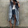 Eine Frau trägt einen hellblauen Tie-Dye-Kimono als Überkleid über einen Jeansminirock vor einer Betonwand.