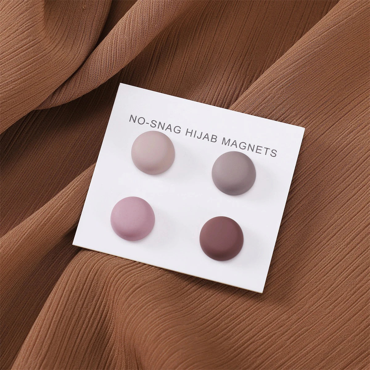 Weiße magnetische Hijab-Pins mit vier matten bunten Pins auf braunem Stoff.