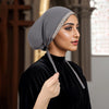 Eine Frau trägt eine graue Hijab-Kappe mit silbernen Strasssteinen und ein schwarzes Rollkragenoberteil.