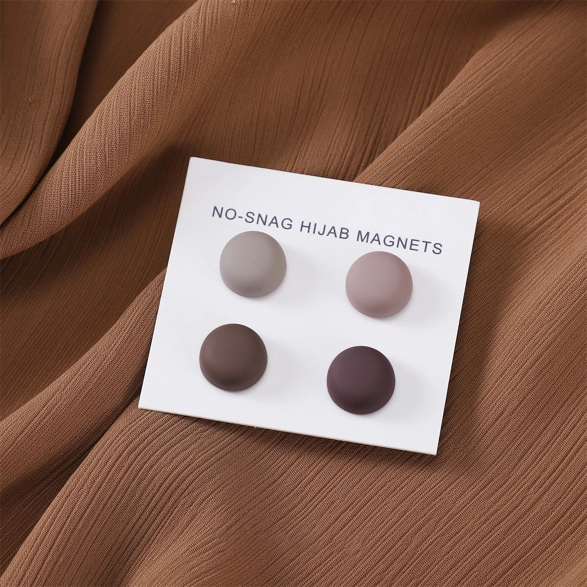 Weiße magnetische Hijab-Nadeln in drei matten Farben auf braunem Stoff.