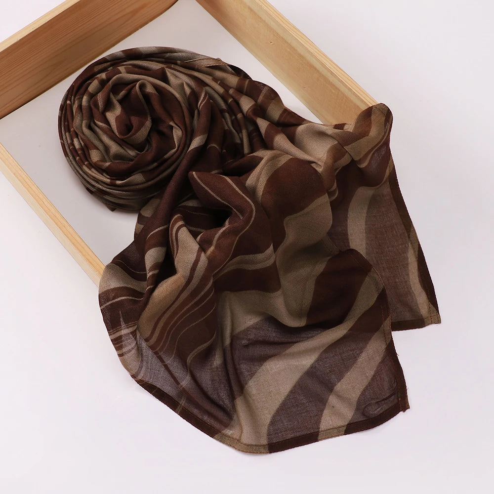 Voile hijab imprimé brun foncé et vert olive roulé et drapé sur un cadre en bois.