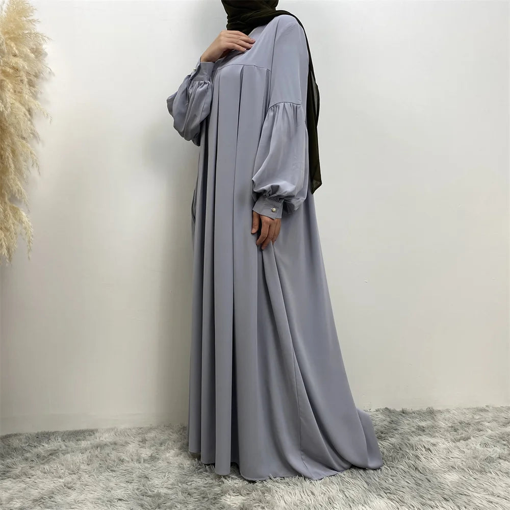 Eine Frau in einem eleganten langen grauen islamischen Kleid mit schwarzem Hijab und gerafften Ärmeln.