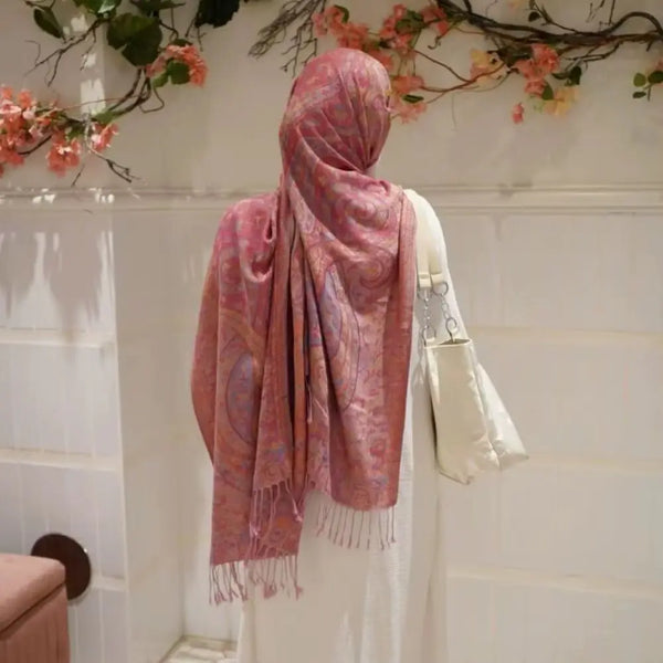 A woman wearing a pink paisley embroidery shawl draped over her shoulder against a white background.