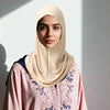 Eine Frau trägt einen beige gefalteten Hijab und ein pinkes gemustertes Oberteil.