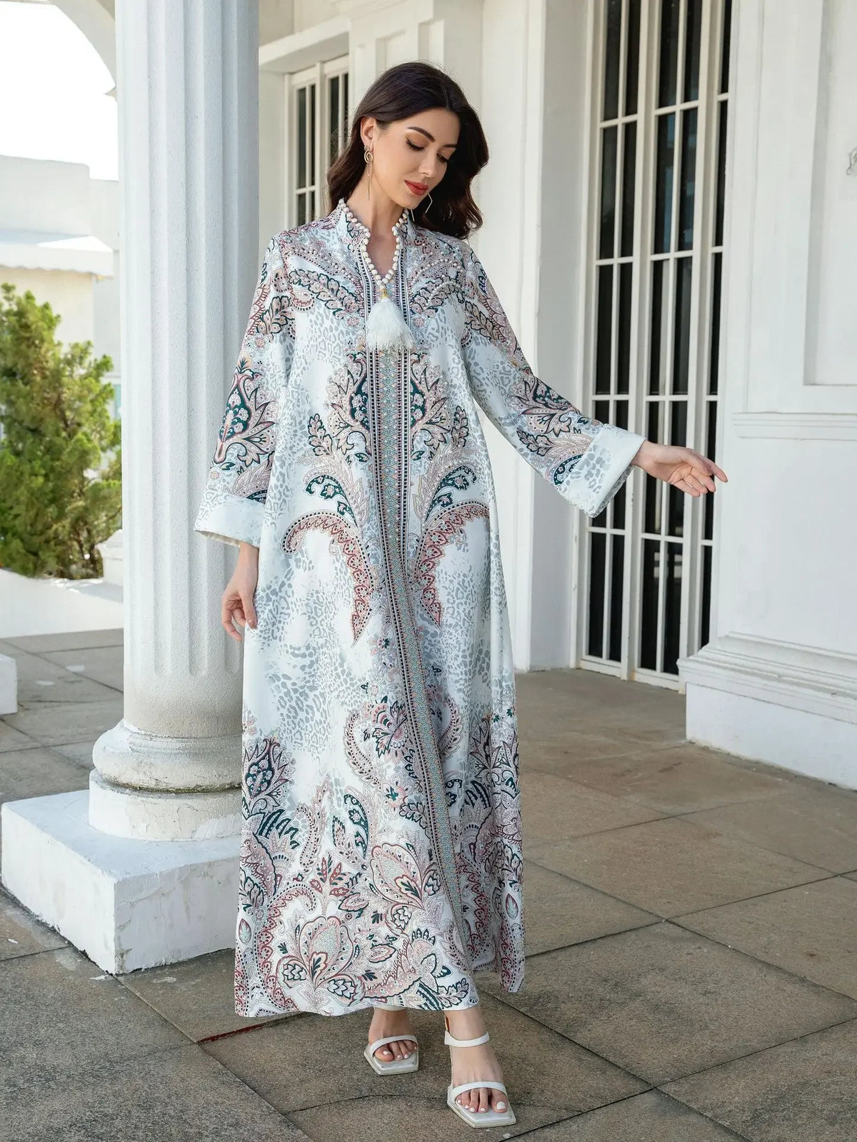 Une femme modélise une élégante abaya perlée en diamant blanche et bleue à motifs floraux, à l'extérieur.