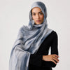 Eine Frau trägt einen hellblauen und grauen aquarellartigen Hijab-Schal über einem schwarzen Oberteil.