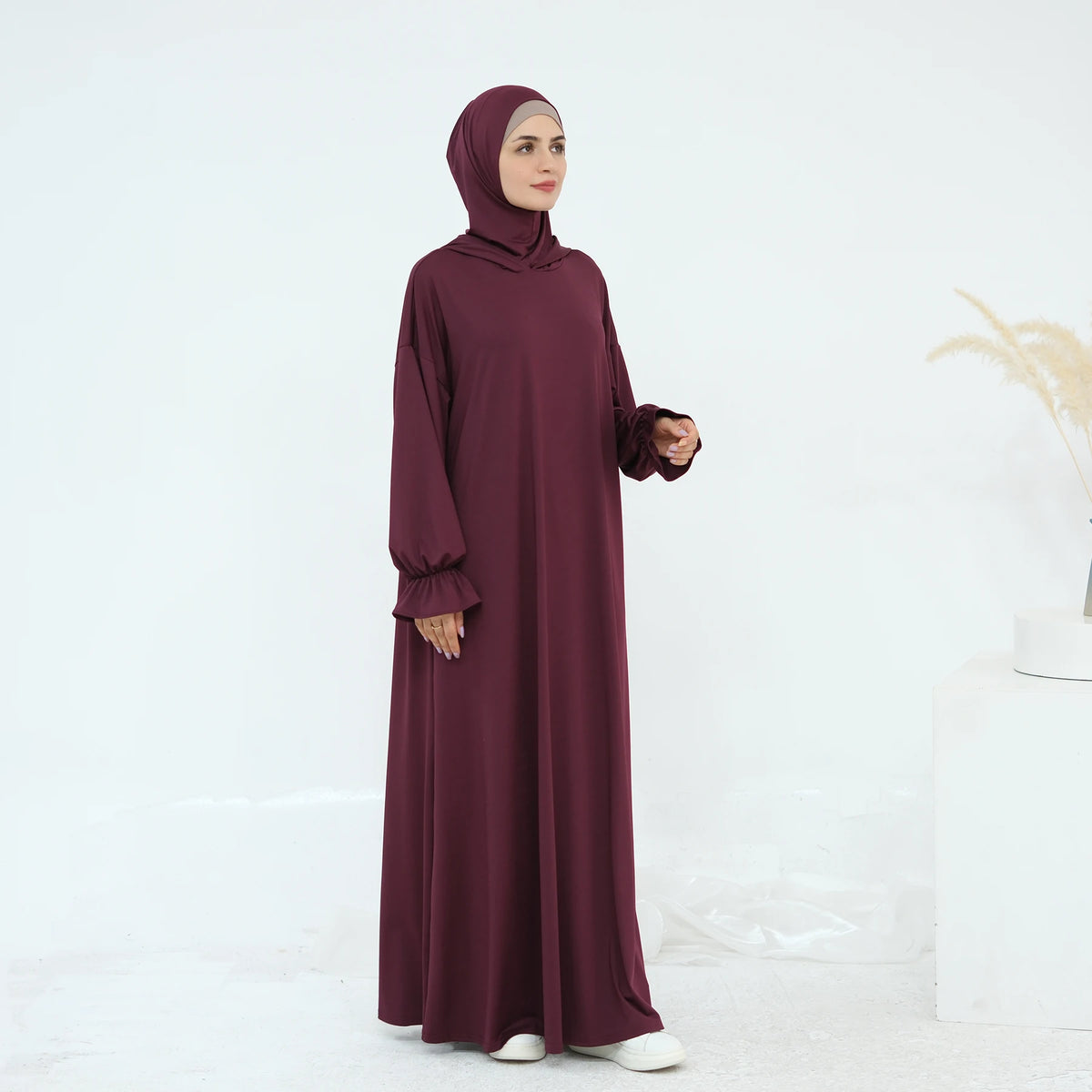 Una mujer vistiendo un vestido abaya holgado y fluido color granate para la oración.