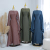 Drei elegante Kaftan-Kleider in Mauve, Olivgrün und staubigem Blau auf Mannequins.
