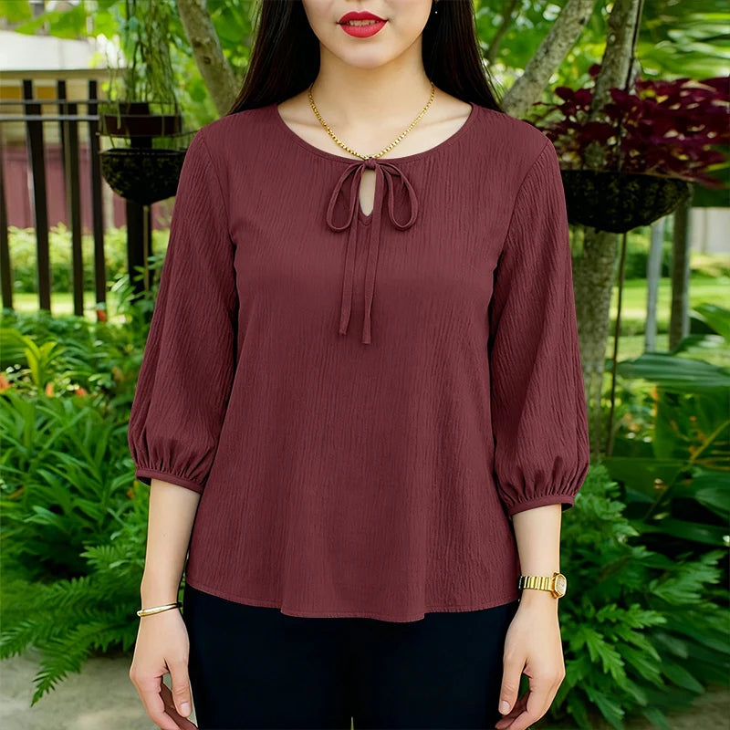 Eine Frau modelliert eine maroonfarbene Spitzenbluse mit gerafften Ärmeln in einer lässigen Outdoor-Umgebung.