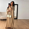 Eine Frau in einem eleganten beige langen Ärmel-Abaya hält eine weiße Handtasche vor einem großen Spiegel.