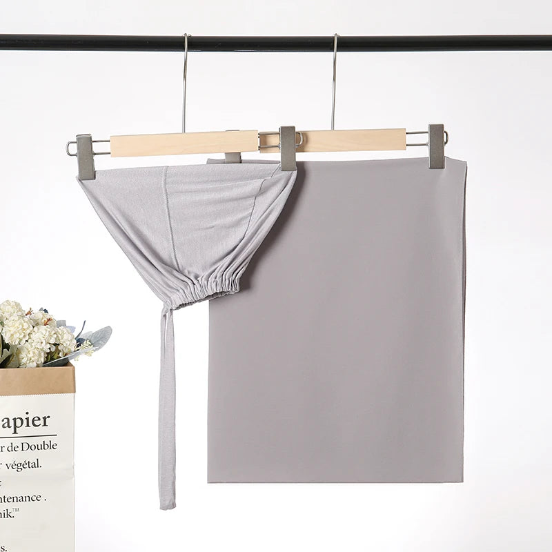 Helles graues Chiffon-Hijab und Untercap-Set an einem Holzstab vor weißem Hintergrund.