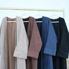 A row of elegant women's abaya trench coats in various neutral and dark colors hanging on a wooden rack.