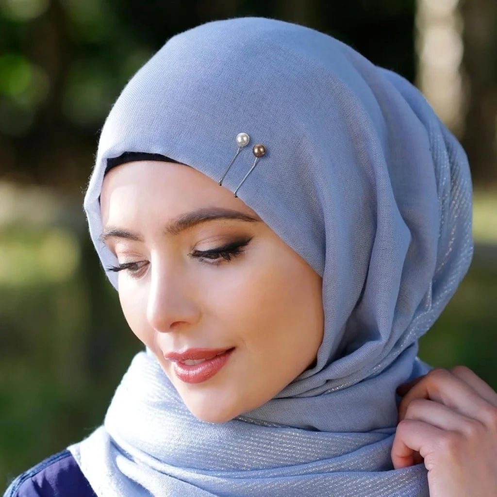 Gros plan d'une femme portant un hijab bleu clair avec des épingles et des accessoires décoratifs.