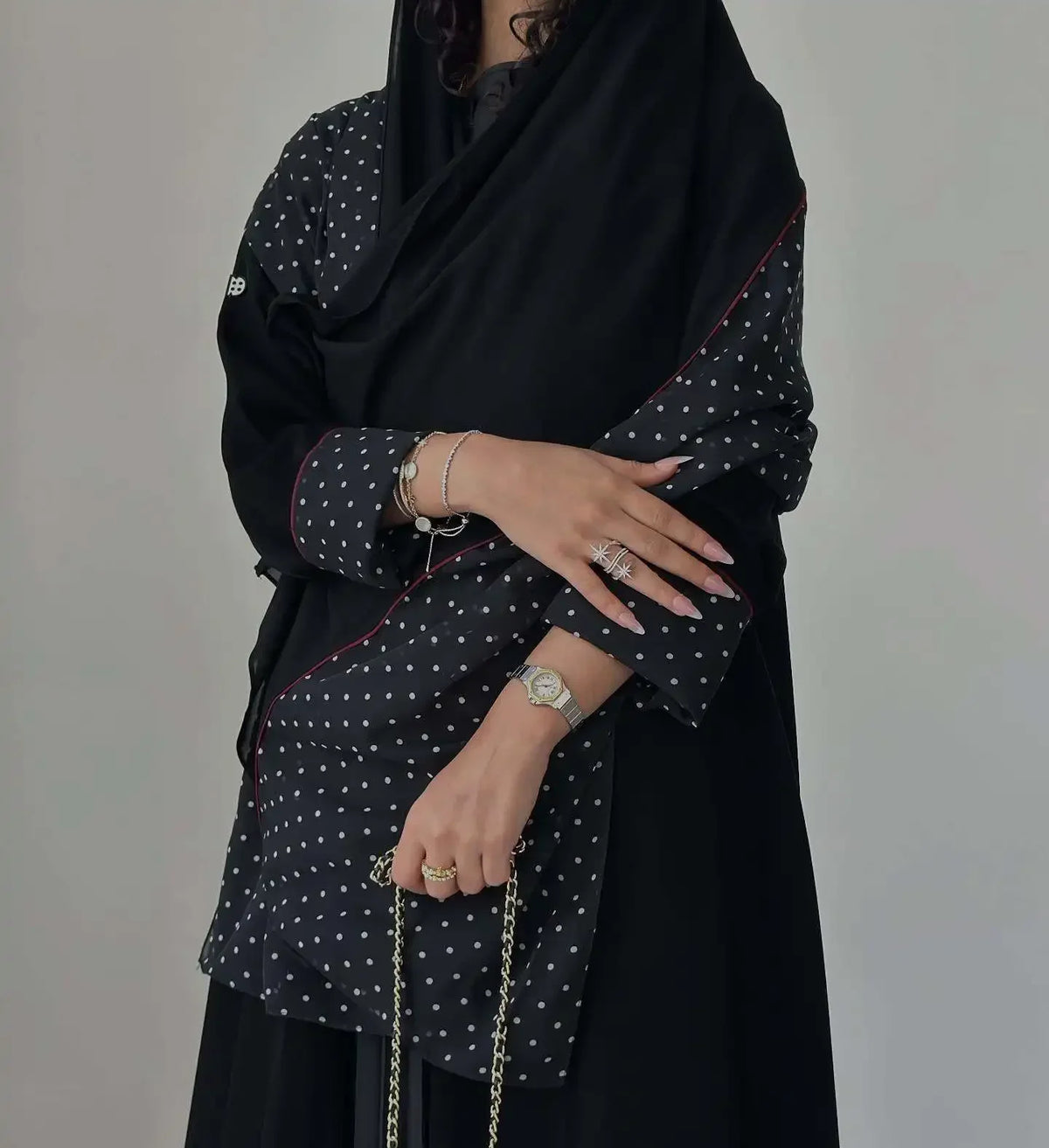 Eine Frau trägt ein elegantes schwarzes Polka-Dot Abaya-Cardigankleid mit goldenen Schmuck.