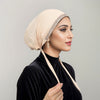 Eine Frau mit beige-Strass-Hijab und schwarzem Oberteil, im Profil dargestellt.
