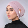 Eine Frau trägt eine staubrosa Jersey-Baumwoll-Hijabkappe und ein schwarzes Rollkragenoberteil.