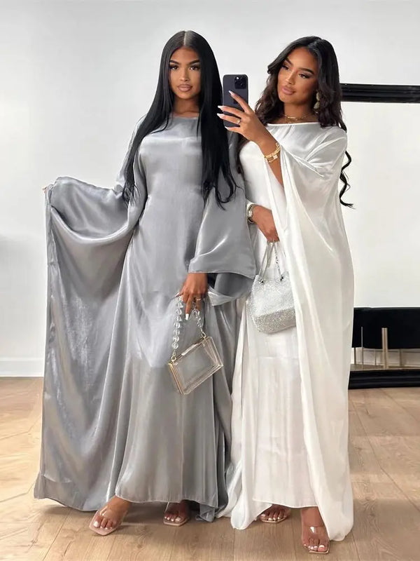 Two women model a silver satin batwing abaya and a white flowing gown.