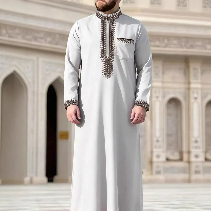Un hombre vistiendo una jubba thobe casual de color gris claro bordada en un entorno arquitectónico ornamentado.
