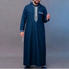 A man wearing a dark blue Moroccan embroidered thobe jellaba with a high collar and silver embroidery.