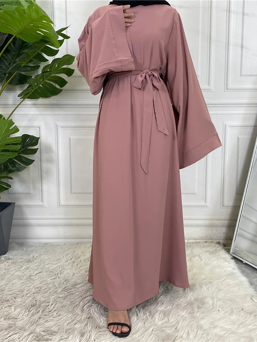 Eleganes mauve maxi Abaya für Damen mit langen Ärmeln und gemachter Taille, präsentiert vor weiß verkleidetem Wandpaneel.