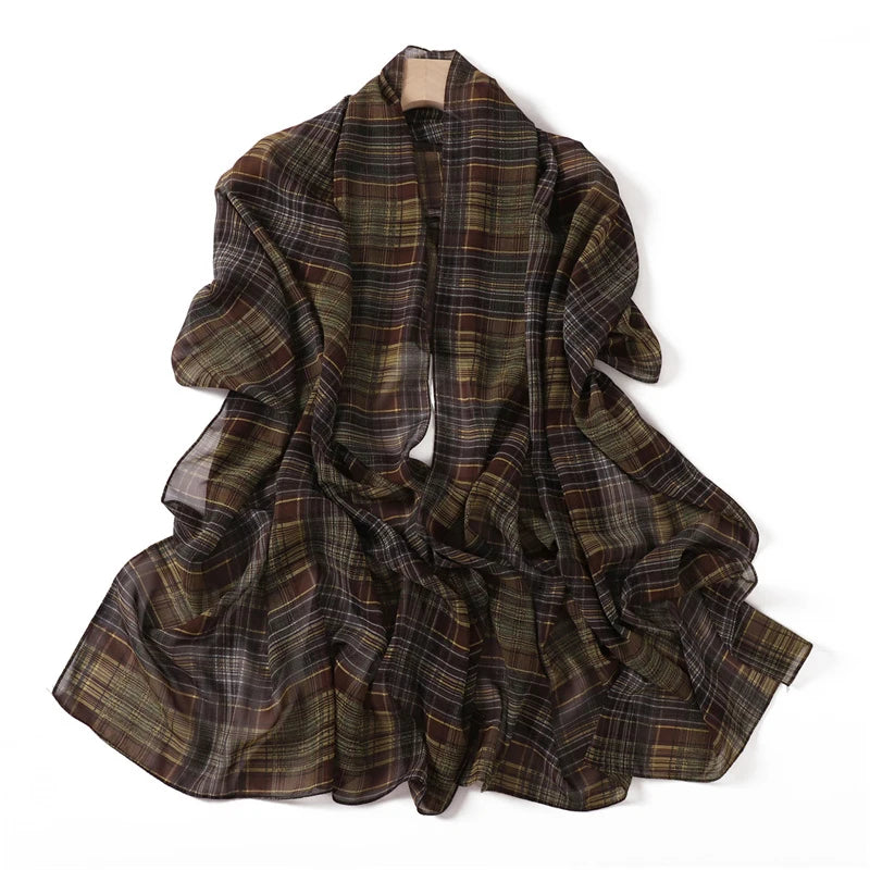 Chal de gasa con estampado de tartán marrón oscuro y oliva colgado en una percha.
