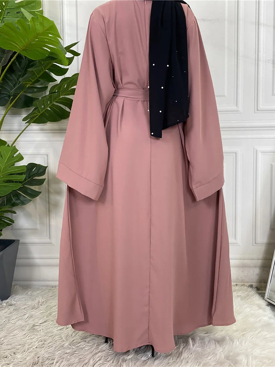 Fließendes, staubrosa Maxi-Abaya für Damen mit schwarzem Zierrand und Ärmeln, vor weißem Hintergrund.