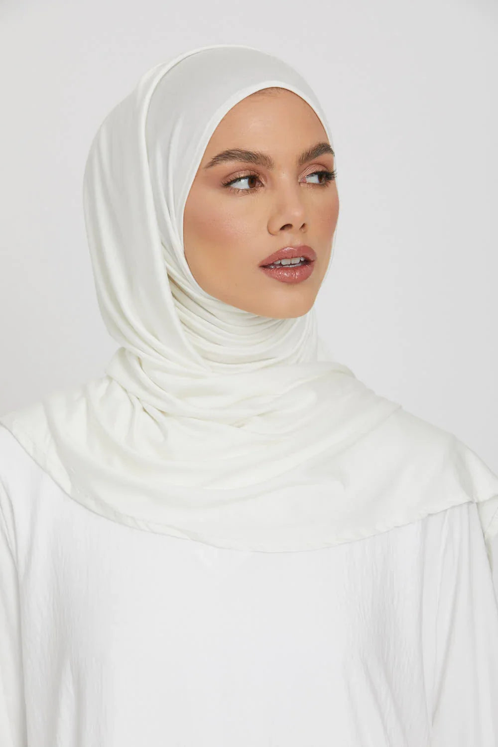 Eine Frau mit weißem Jersey-Hijab-Schal, die zur Seite blickt.