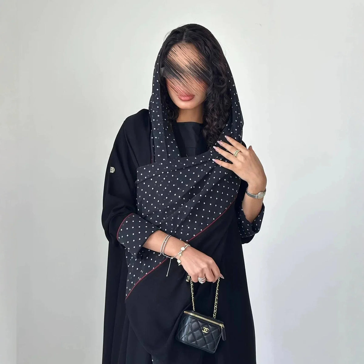 Eine Frau trägt ein elegantes schwarzes Abaya-Cardigan-Kleid mit Polka-Dot-Muster und Kapuze.
