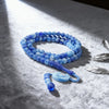 Una hebra de cuentas de vidrio azul usada como tasbih de oración con borlas de luna y estrella sobre tela blanca.
