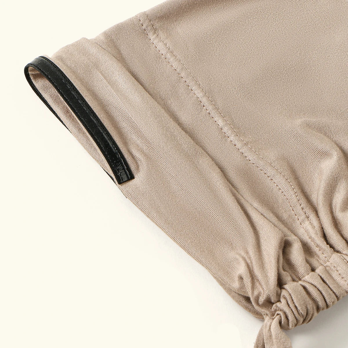 A close-up of a beige anti-slip inner hijab cap with a black trim and gathered fabric detail.
