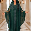 Una mujer modela un abaya maxi fluido verde oscuro con mangas de murciélago en un interior bien iluminado.