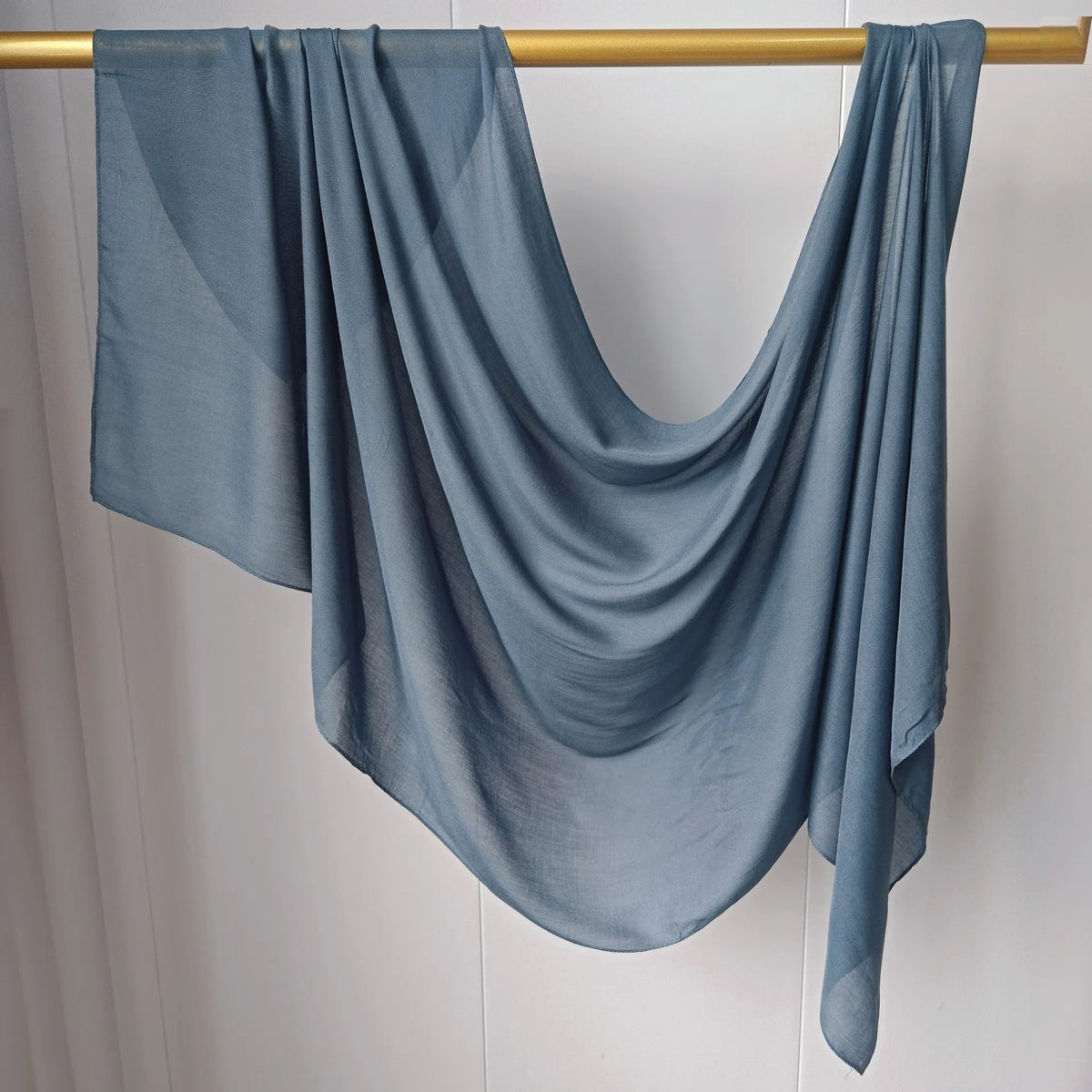 Foulard hijab bleu-gris solide et fluide drapé sur un cintre en bois.