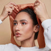 A woman is adjusting an elegant satin hijab cap and undercap set on her head.