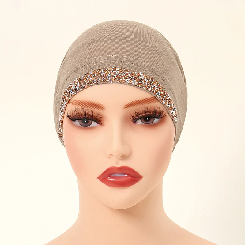 Modelo usando un hiyab elástico beige decorado con bordado de purpurina dorada en la frente.