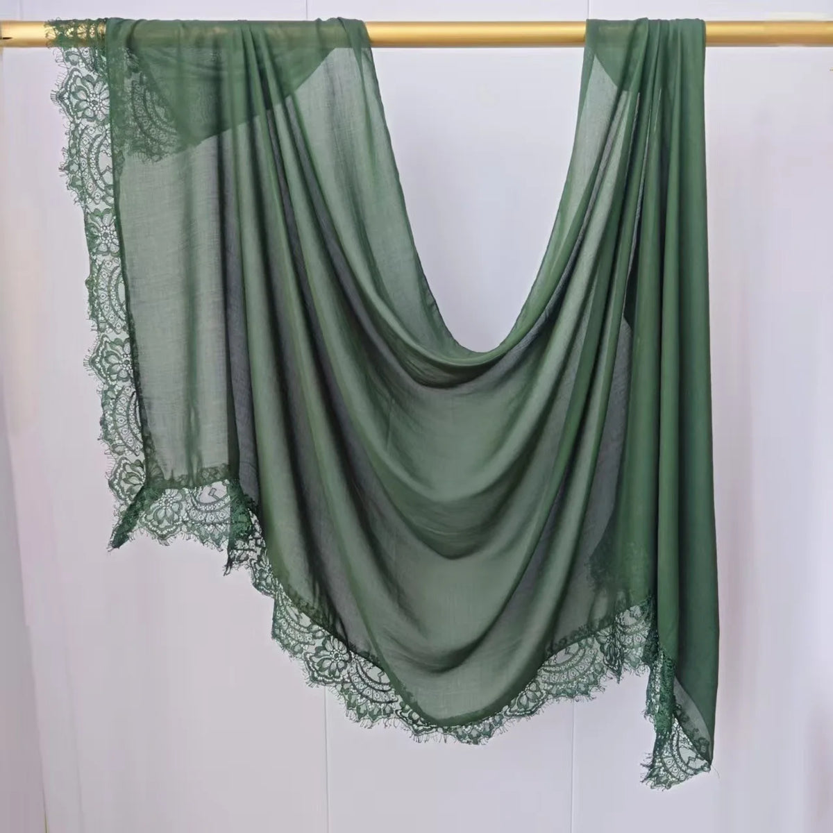 Hijab de gasa verde oliva modal colgado en un perchero de madera.